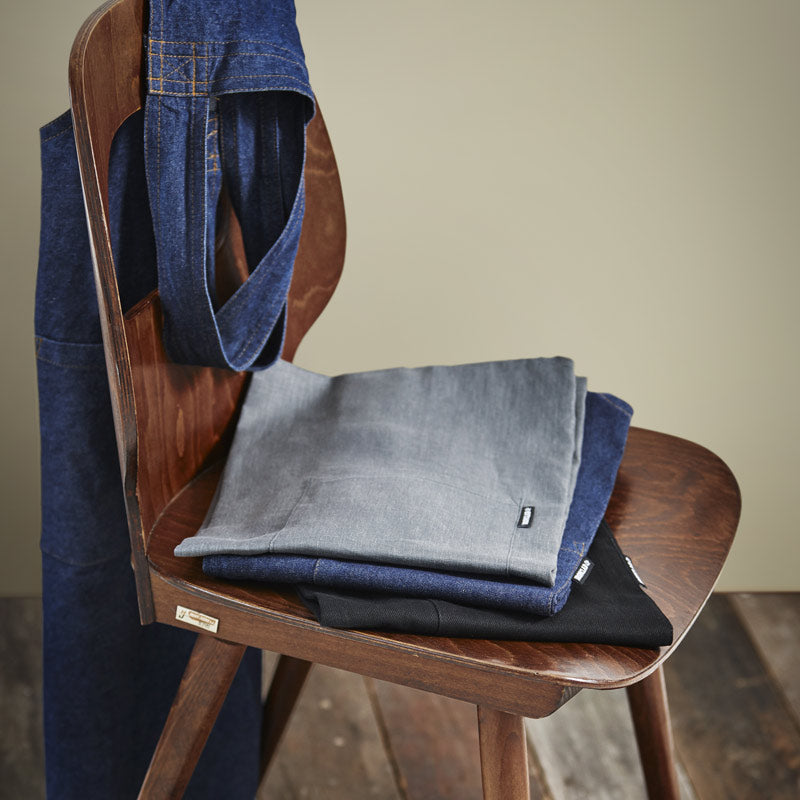 The Master Aprons sitting in a stack on a wooden chair with one draped over the back